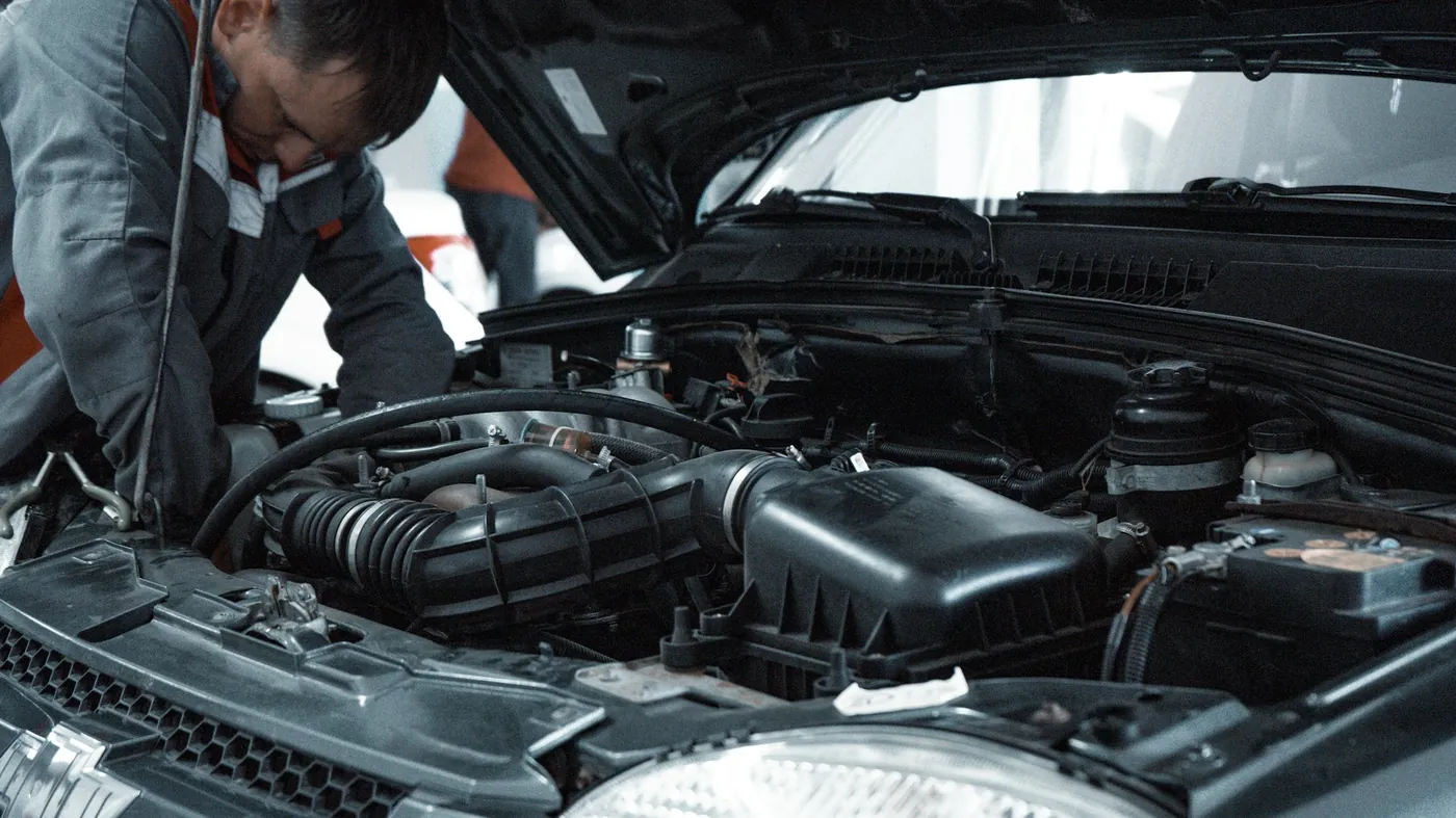Mechanic working under an open hood. Illustrative photo.